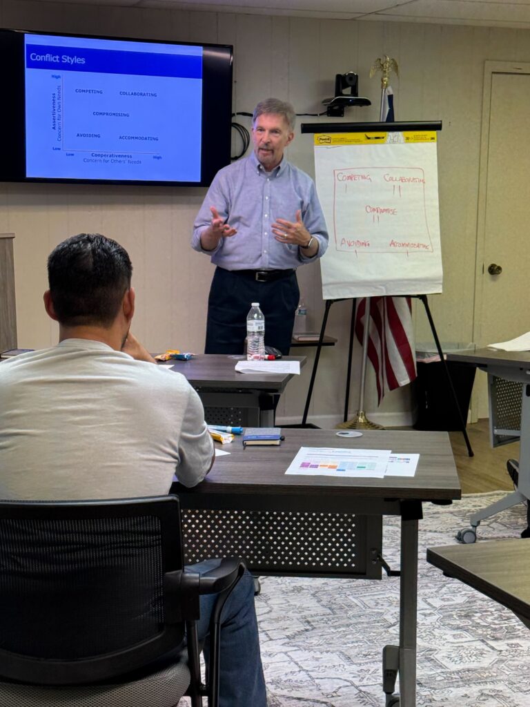 Leadership trainer explaining conflict styles using a flip chart and presentation screen during a hands-on supervisor training session.